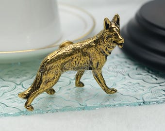 May include: A gold-colored metal German Shepherd dog figurine. The figurine is standing on a light blue glass surface.