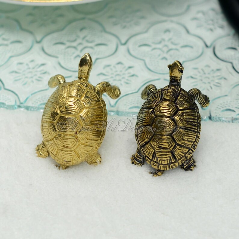 May include: Two small gold turtle figurines with detailed shell patterns. The turtles are facing opposite directions.