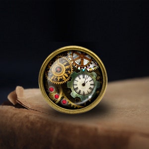 May include: A round, brass-coloured pendant with a glass dome featuring a steampunk design of gears and a clock face. The clock face has Roman numerals and a red second hand.