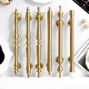 Puede incluir: Una colecci&oacute;n de seis manijas de puerta doradas con varios dise&ntilde;os ornamentados. Cada manija presenta una placa trasera decorativa para el montaje. Las manijas var&iacute;an en longitud y estilo, mostrando una gama de dise&ntilde;os elegantes de inspiraci&oacute;n vintage.