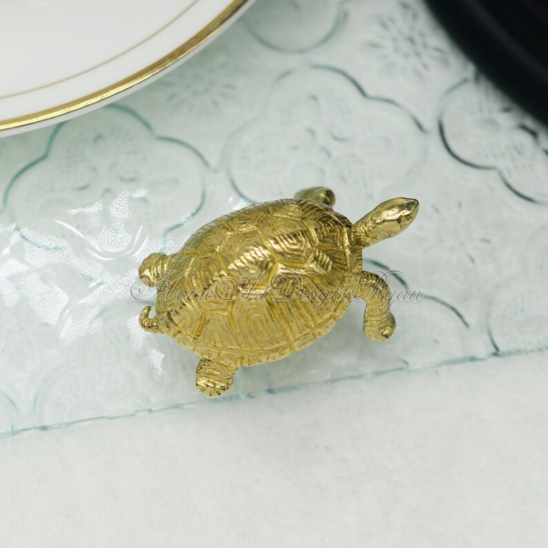 May include: A small gold turtle figurine. The turtle is sitting on a clear glass surface.