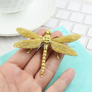 May include: A gold-coloured dragonfly brooch with detailed wings and a textured body.