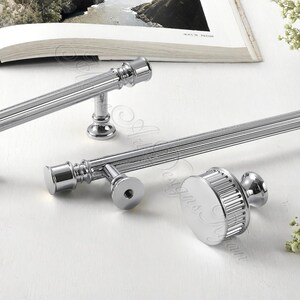 Puede incluir: Primer plano de varias piezas de herrajes de gabinete cromados pulidos. Los herrajes incluyen tiradores de barra largos y un pomo redondo, todos con un dise&ntilde;o acanalado. Las piezas est&aacute;n dispuestas sobre una superficie blanca, lo que sugiere un tema de decoraci&oacute;n del hogar.