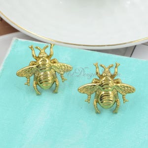 May include: Two gold bee-shaped decorative drawer pulls. The bees have detailed wings and legs.