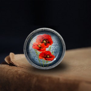 May include: A silver knob with a glass top featuring a floral design of three red poppies on a blue background.