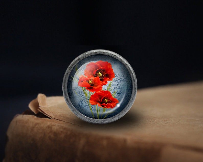 May include: A silver knob with a glass top featuring a floral design of three red poppies on a blue background.