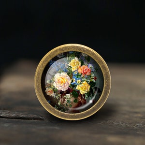 May include: A round, brass-coloured pendant with a glass insert featuring a vintage painting of a bouquet of colourful flowers.