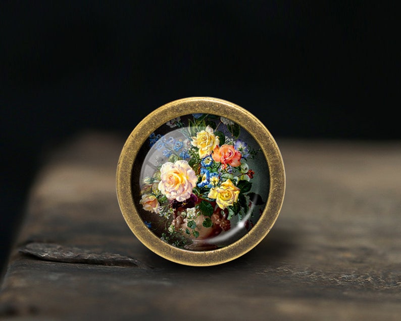 May include: A round, brass-coloured pendant with a glass insert featuring a vintage painting of a bouquet of colourful flowers.