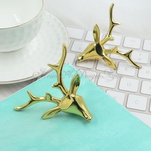 Può includere: Due sculture dorate di testa di cervo con corna. Le sculture sono su una superficie blu chiaro e una tastiera bianca.