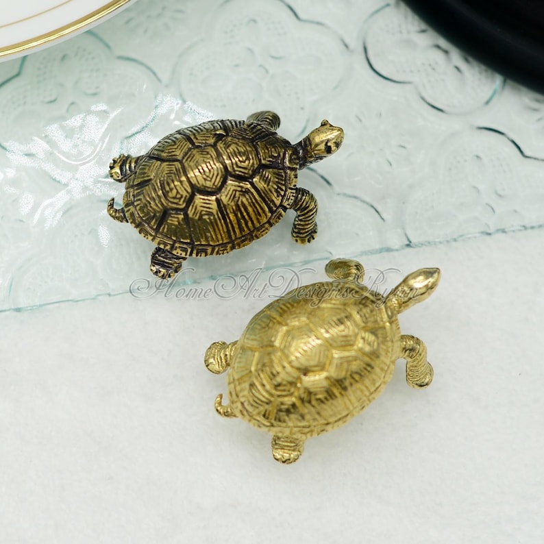 May include: Two small gold-colored turtle figurines. The turtles are detailed with a textured shell and are facing different directions.