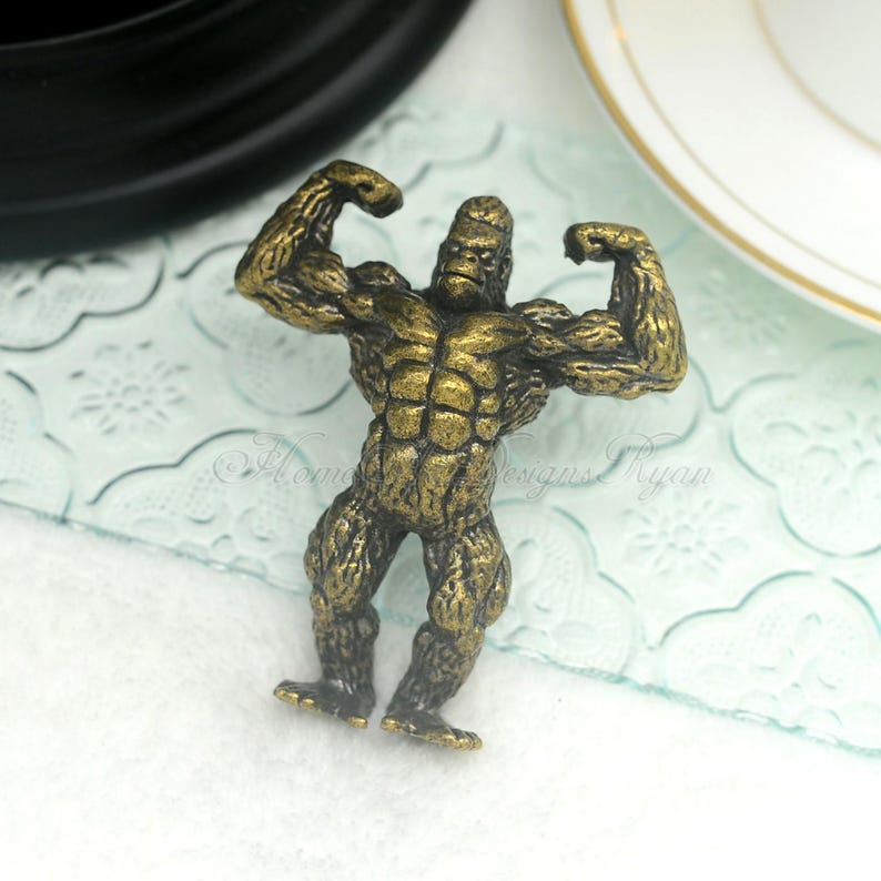 Pu&ograve; includere: Una statuetta di metallo dorata di un gorilla che flette i bicipiti. Il gorilla &egrave; in piedi su una superficie bianca.