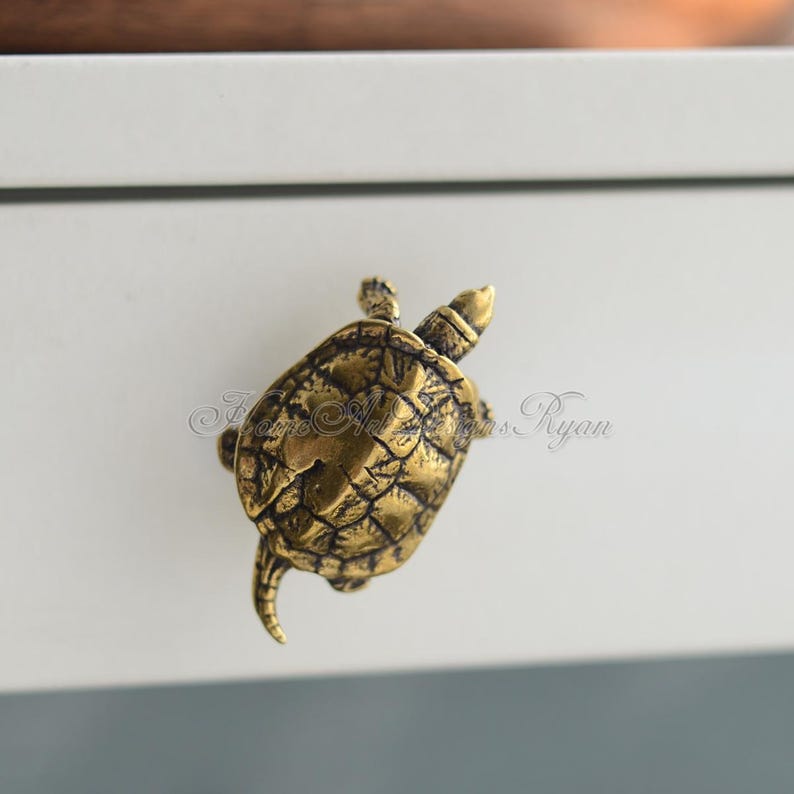 May include: A gold-toned turtle drawer pull. The turtle is facing to the right and has a detailed shell.