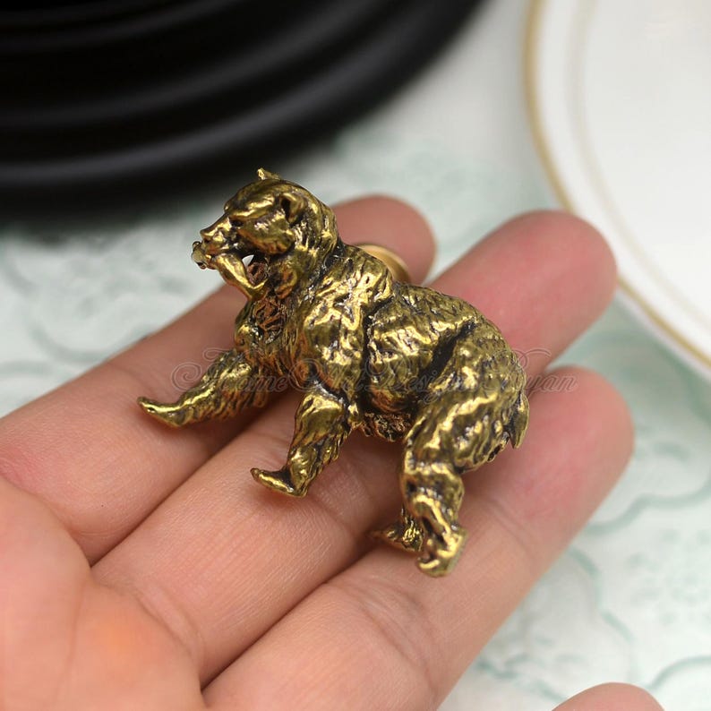 May include: A gold-toned metal bear figurine with a detailed, textured surface. The bear is standing on all fours and has a slightly aggressive expression.