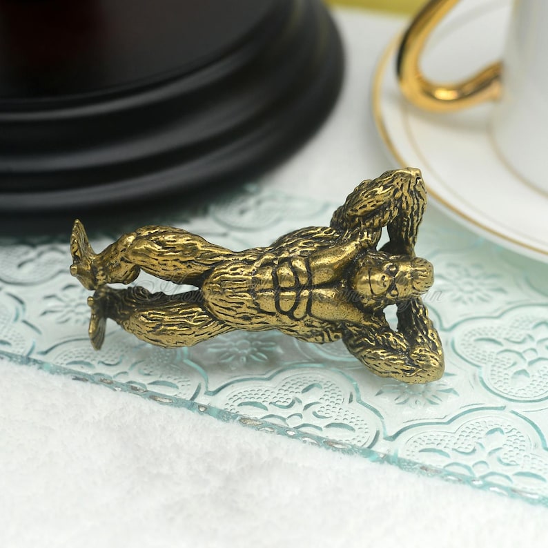 Op de afbeelding: Een gedetailleerd, goudkleurig gorillafiguur in een ontspannen pose. De sculptuur heeft ingewikkelde texturen en ligt op een helder, patroonrijk oppervlak. De armen van de gorilla zijn gebogen en zijn benen zijn uitgestrekt.