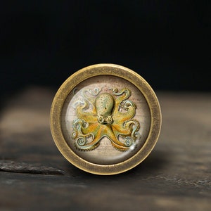 May include: A brass knob with a glass insert featuring an illustration of an octopus with yellow and green tentacles on a white background.
