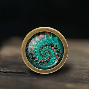Peut inclure: Un pendentif rond de couleur laiton avec un motif en spirale vert et rose à l'intérieur d'un dôme en verre.