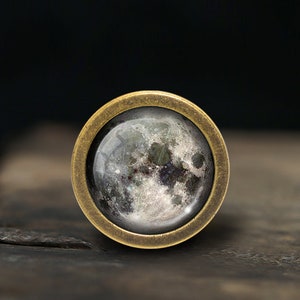 May include: A brass ring with a glass cabochon featuring a detailed image of the moon.