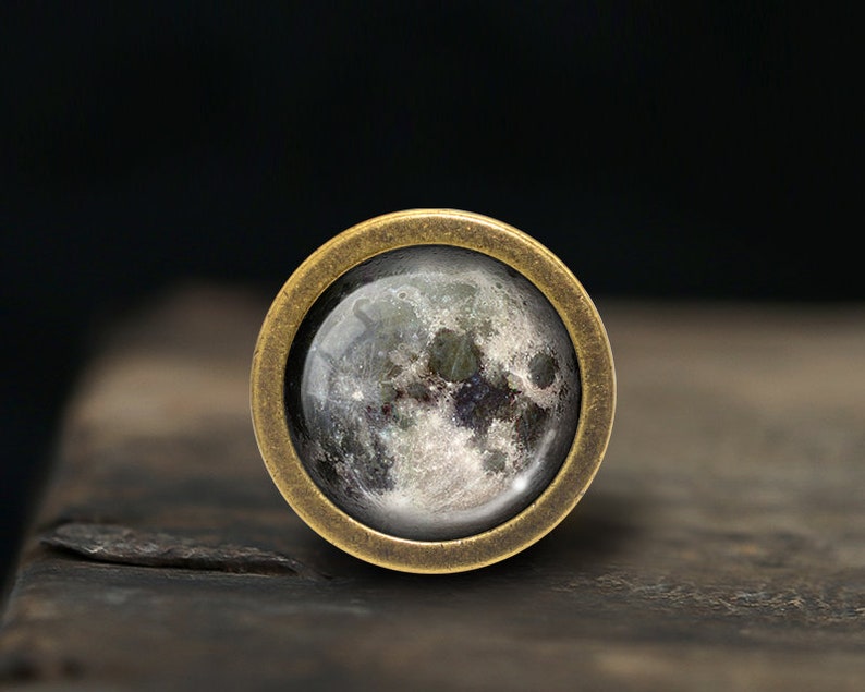 Puede incluir: Un anillo de lat&oacute;n con un cabuj&oacute;n de vidrio que presenta una imagen detallada de la luna.