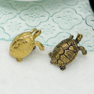 May include: Two gold turtle figurines, one facing forward and the other facing backward, on a white surface.