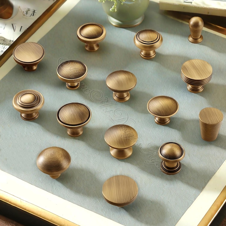 Puede incluir: Una colecci&oacute;n de tiradores de armario de lat&oacute;n antiguo en varias formas y tama&ntilde;os. Los tiradores tienen un acabado c&aacute;lido y envejecido, con dise&ntilde;os que van desde c&uacute;pulas simples hasta estilos detallados y en capas. La disposici&oacute;n sugiere una exhibici&oacute;n de opciones de hardware.