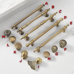 May include: A selection of antique brass cabinet hardware, including pull handles and knobs. The pulls vary in length, and the knobs feature different decorative designs. The hardware is arranged on a white surface.