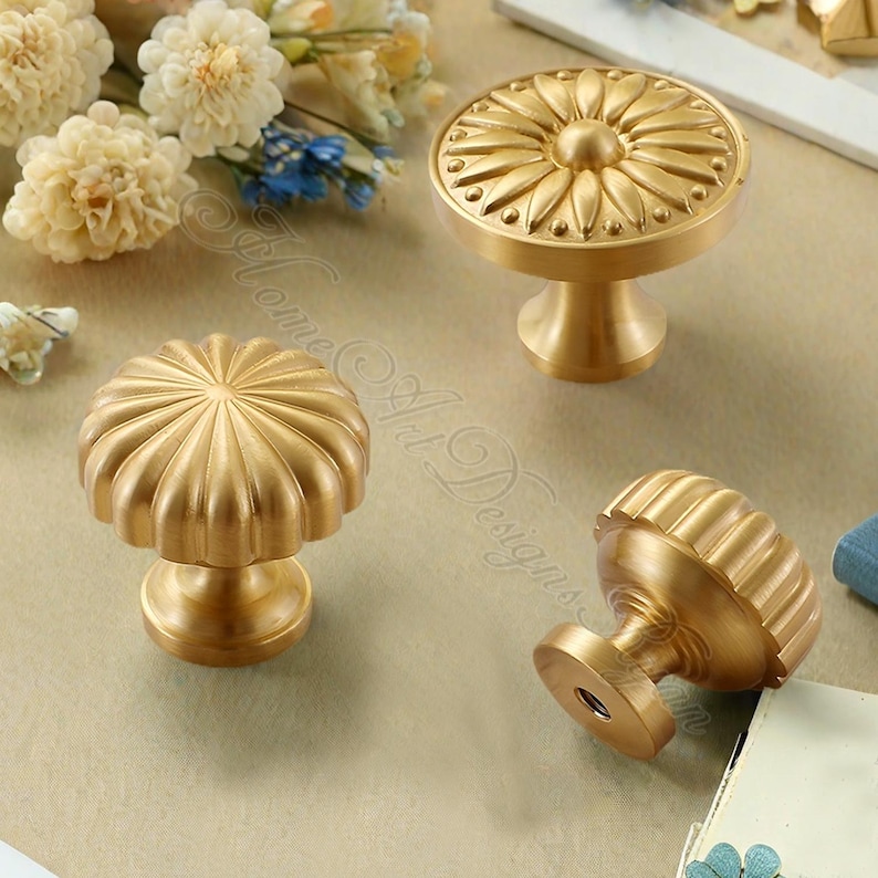 Puede incluir: Cuatro tiradores dorados para armarios con dise&ntilde;os decorativos. Dos tiradores tienen un patr&oacute;n similar a un girasol, y dos tienen un dise&ntilde;o acanalado en forma de calabaza. Los tiradores son de metal y tienen un estilo cl&aacute;sico y elegante.