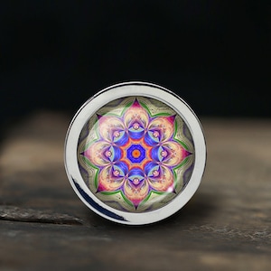 May include: A circular button with a silver-coloured rim and a vibrant mandala design. The mandala features a symmetrical pattern with blue, pink, orange, and green hues. The button has a shiny, metallic border and a slightly domed, glass-like centre.