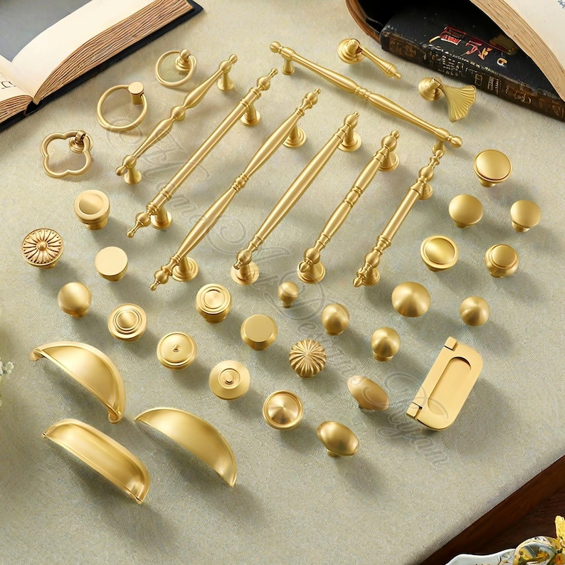 Puede incluir: Una colecci&oacute;n de herrajes dorados para gabinetes, que incluyen perillas, tiradores y manijas. Los herrajes presentan varios dise&ntilde;os, desde perillas redondas simples hasta tiradores ornamentados con detalles decorativos.