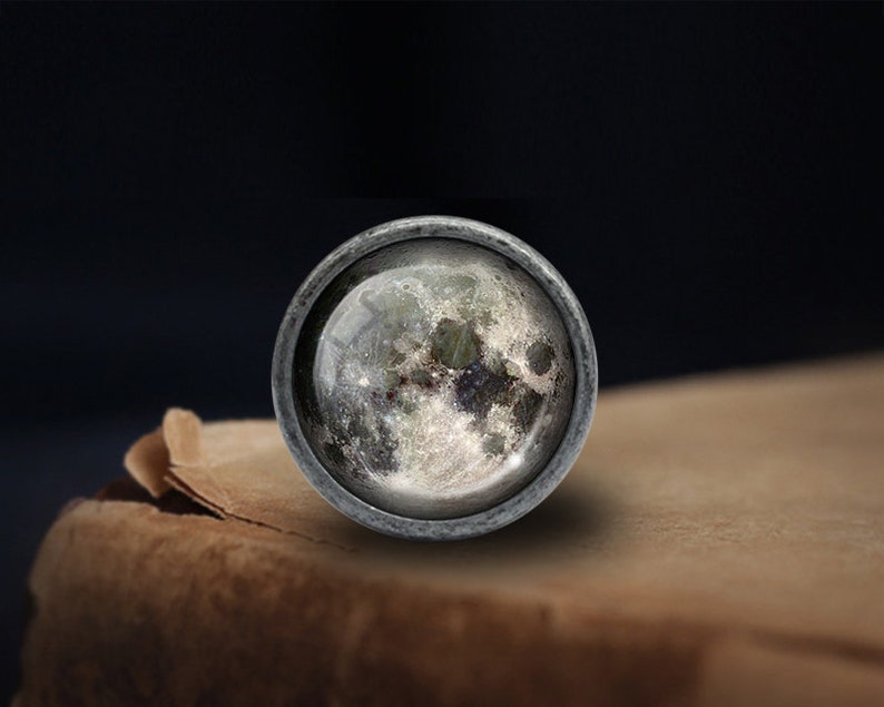 Puede incluir: Un pomo redondo plateado con un inserto de vidrio que presenta una imagen detallada de la superficie de la luna.