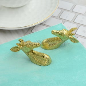 May include: Two gold-colored deer head figurines on a turquoise surface. The deer heads are facing different directions.