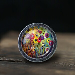 May include: A round, silver-toned knob with a colorful abstract floral design. The design features a field of flowers with yellow, red, blue, and purple petals. The knob is perfect for adding a touch of whimsy to any room.