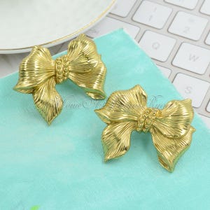 May include: A pair of gold-tone bow-shaped earrings with a beaded accent in the center.