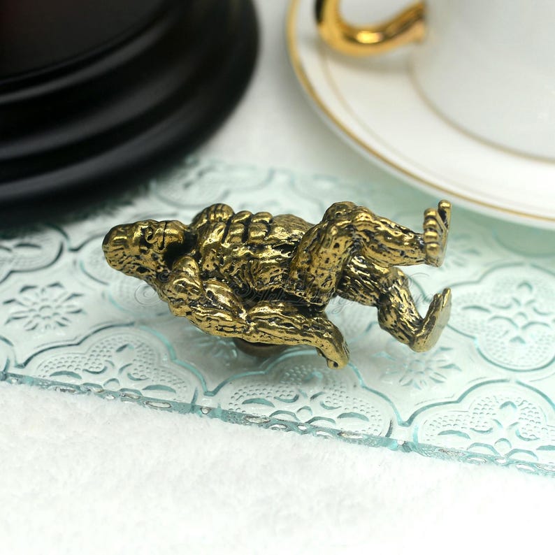 K&ouml;nnte beinhalten: Eine goldfarbene Metallfigur eines liegenden Gorillas. Die Figur ist mit Fell detailliert und hat eine entspannte Pose.