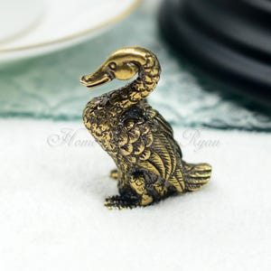 May include: A small, gold-colored metal figurine of a duck with detailed feathers. The duck is sitting with its head turned to the side.