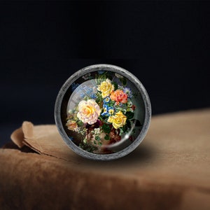 May include: A silver-toned knob with a glass insert featuring a colourful floral arrangement of yellow, pink, and blue roses in a vase.