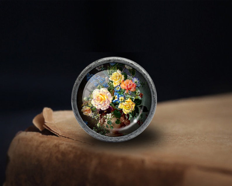 May include: A silver-toned knob with a glass insert featuring a colourful floral arrangement of yellow, pink, and blue roses in a vase.