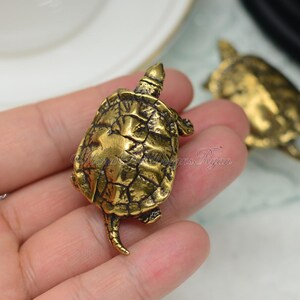 May include: Two gold-colored turtle figurines. The turtle on the left is facing the right and the turtle on the right is facing the left. Both turtles have detailed shell textures.