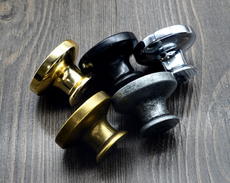 Pode incluir: Quatro bot&otilde;es de arm&aacute;rio em diferentes acabamentos: dourado, preto, prata e lat&atilde;o envelhecido. Os bot&otilde;es s&atilde;o redondos com um centro elevado e uma superf&iacute;cie lisa.