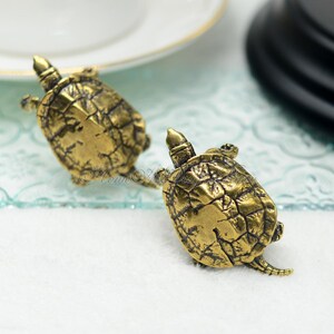 May include: Two gold-toned turtle figurines. The turtles are detailed with textured shells and are facing opposite directions.