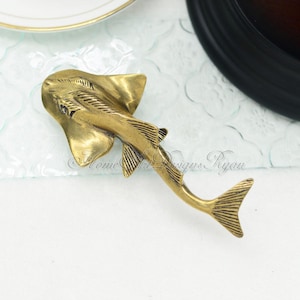 Peut inclure: Une sculpture en métal de couleur dorée représentant une raie. La sculpture est détaillée avec des lignes et des rainures pour créer une texture réaliste.