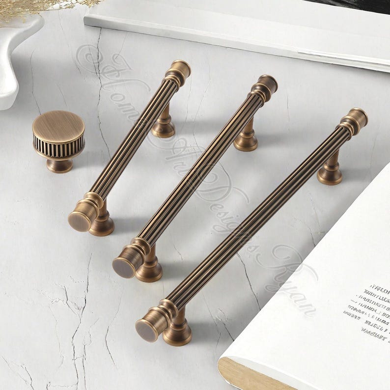 Puede incluir: Un juego de herrajes de gabinete de bronce antiguo, que incluye tres tiradores largos y un pomo redondo. Los tiradores tienen un dise&ntilde;o acanalado y son adecuados para cajones o puertas. Los herrajes se exhiben sobre una superficie clara.