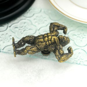 Pu&ograve; includere: Un pomello per armadio in metallo dorato a forma di gorilla con le braccia flesse. Il gorilla &egrave; in posizione accovacciata.