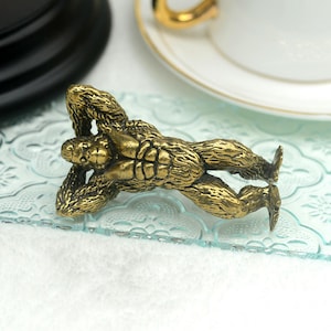 Op de afbeelding: Een gedetailleerd, goudkleurig gorillafiguur in een liggende houding. De gorilla ligt op zijn rug met zijn armen boven zijn hoofd. Het beeldje staat op een helder, getextureerd oppervlak.