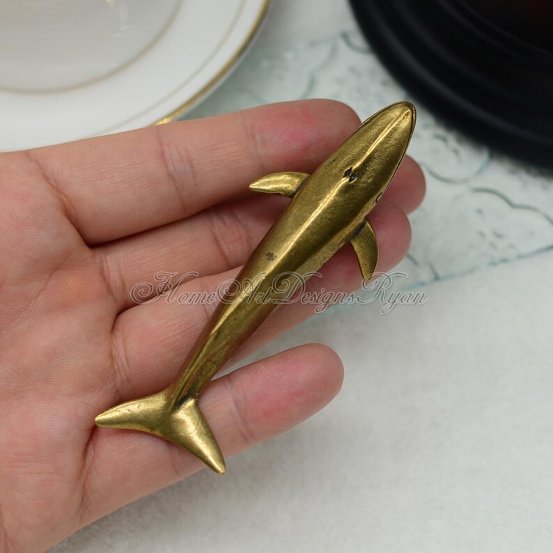 May include: A gold-colored metal whale figurine. The whale is facing to the right and has a smooth, polished finish.