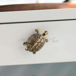May include: A gold-colored turtle drawer pull. The turtle is facing right and has a detailed shell.