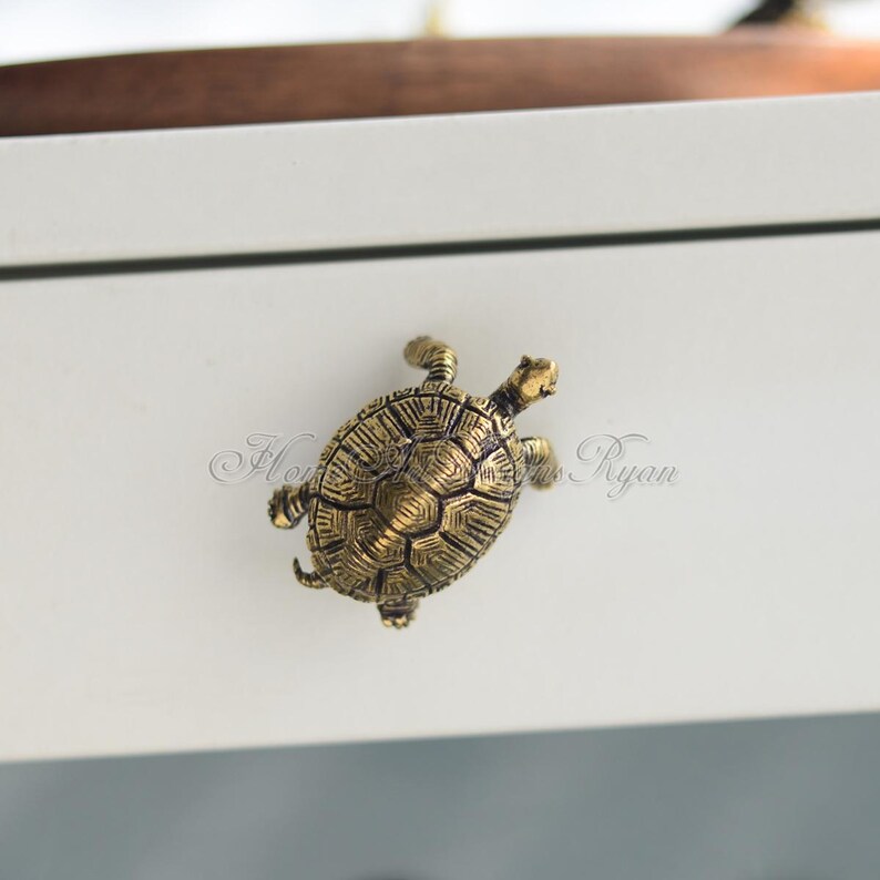 May include: A gold-colored turtle drawer pull. The turtle is facing right and has a detailed shell.