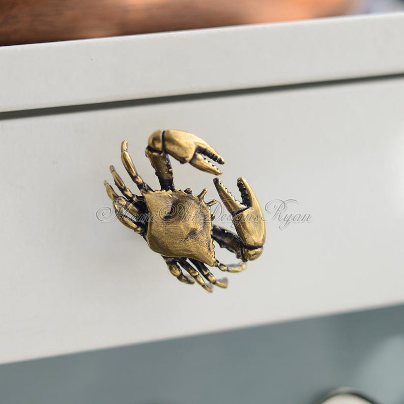 Puede incluir: Un tirador de caj&oacute;n en forma de cangrejo de color dorado. El cangrejo est&aacute; detallado con patas y garras texturizadas.