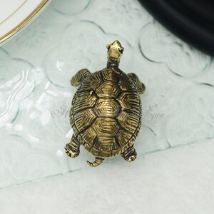 May include: A small, gold-colored turtle figurine with a detailed shell. The turtle is facing forward with its head raised.