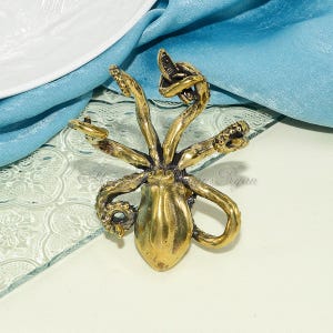 May include: A gold-colored octopus figurine with a detailed design. The octopus has eight tentacles and is positioned on a glass surface with a decorative pattern.