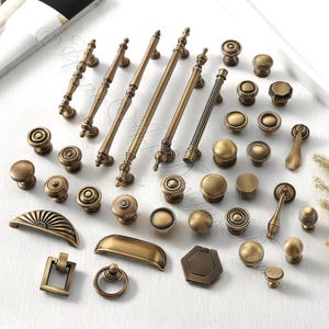 以下が含まれることがあります： アンティーク真鍮製のキャビネット金具の詰め合わせ。ノブ、プル、ハンドルが含まれています。シンプルな丸いノブから装飾的なディテールが施された華やかなプルまで、さまざまなデザインがあります。白い表面に配置されています。